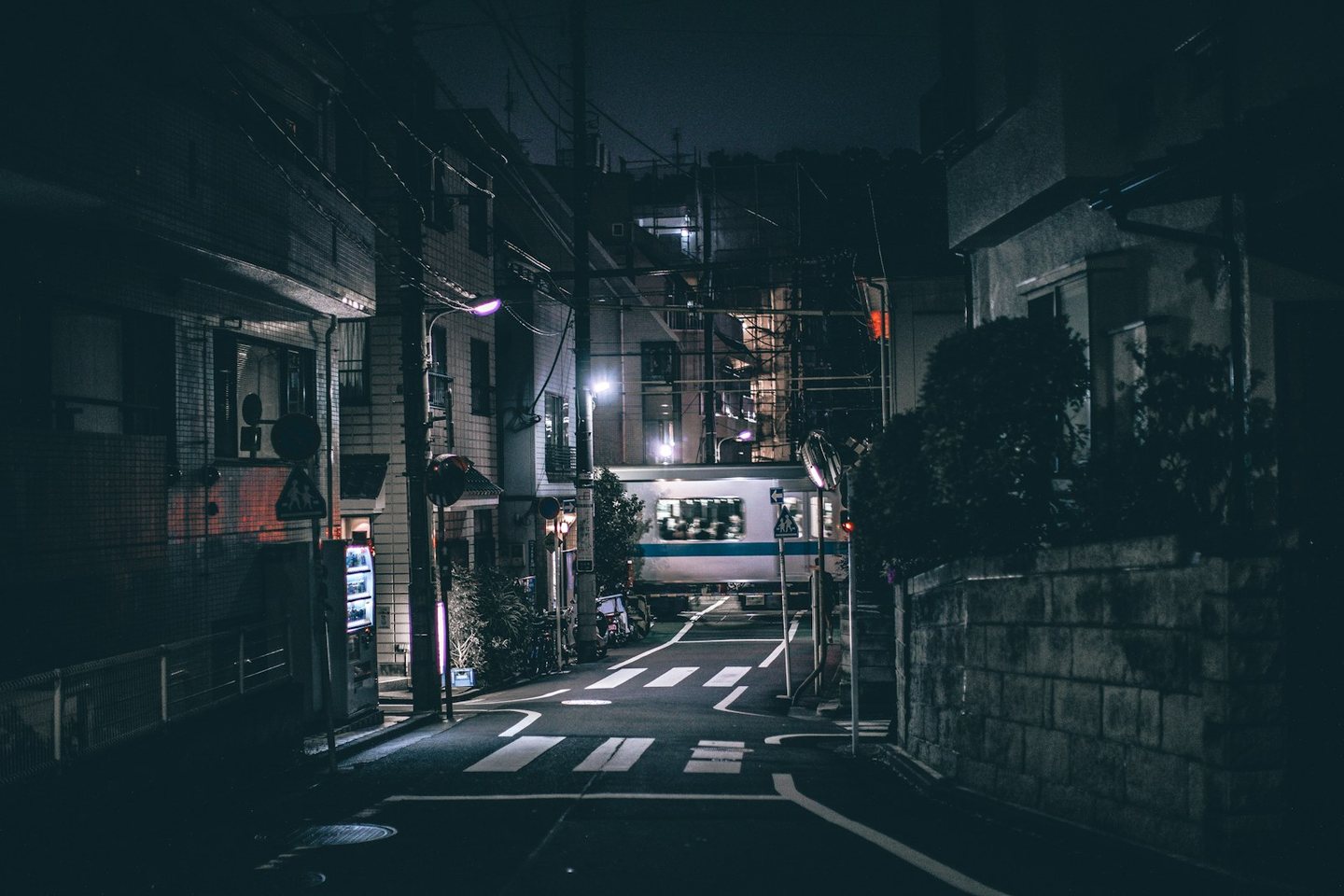 A quiet Tokyo backstreet at night, a train passing at a level crossing